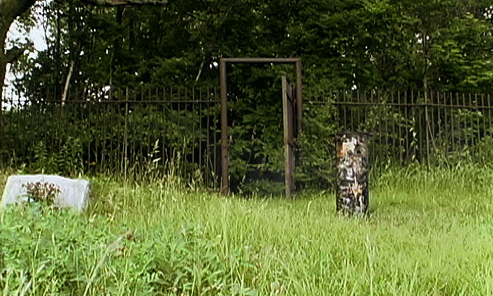 An overgrown gate to a graveyard.